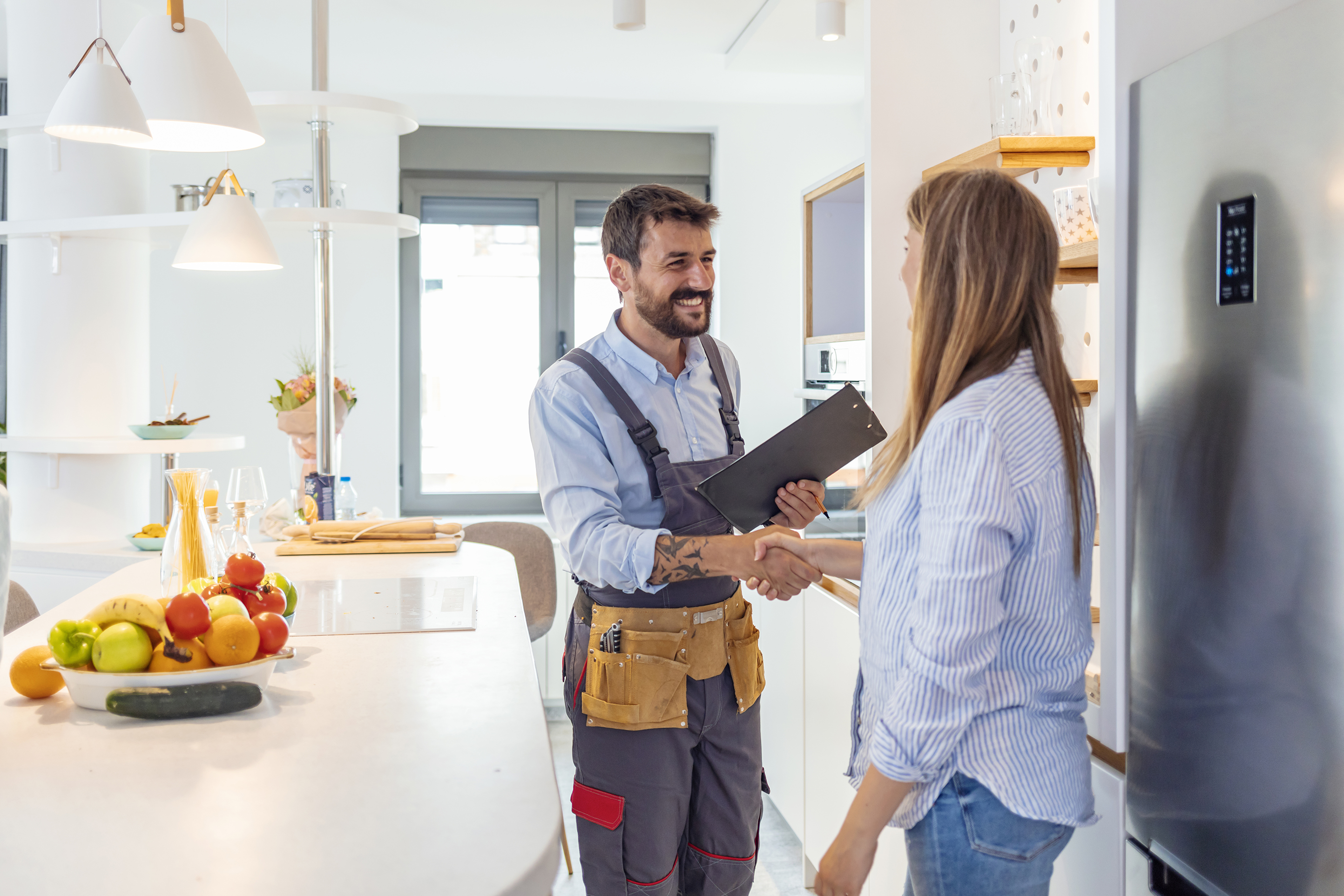 Young woman shaking hands with male contractor with clipboard in kitchen